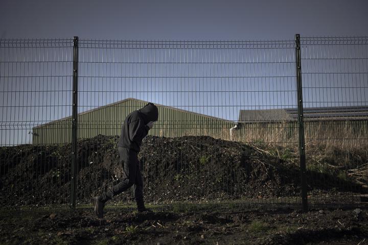 Hooded youth walks past abandoned buildings on waste land