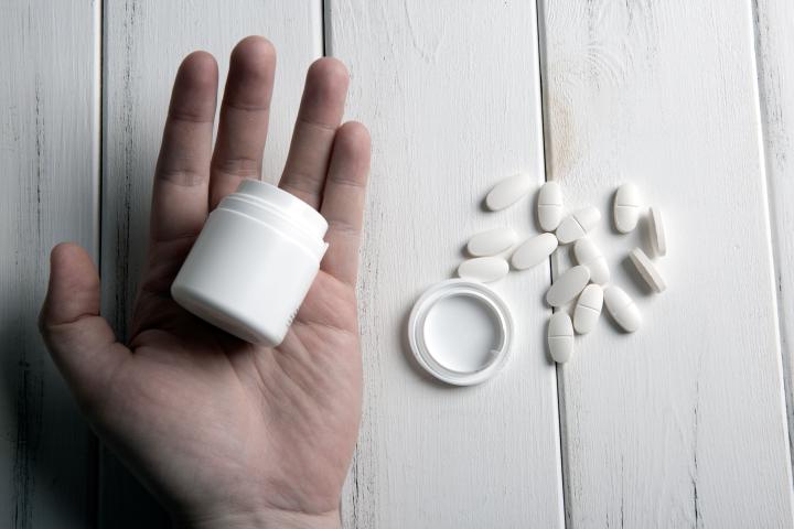 White pills and a jar in human hand on a wooden table