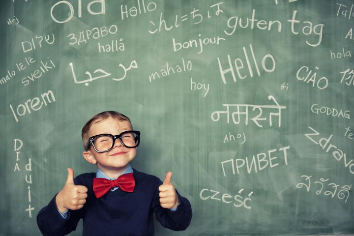 Boy with glasses in front of blackboard with foreign languages written on it