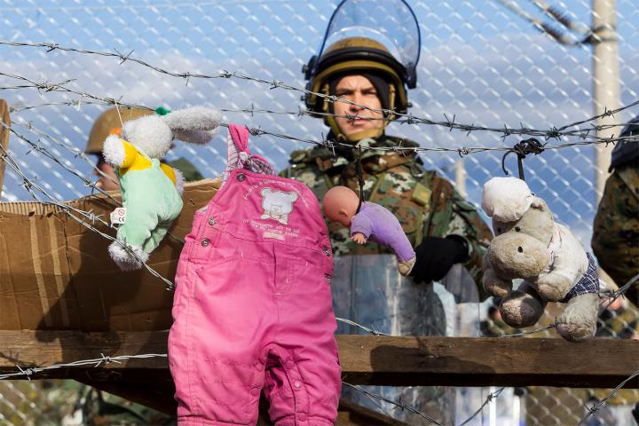 A solider in full kit, standing behind barbed wire that has childrens clothes hanging from it. 