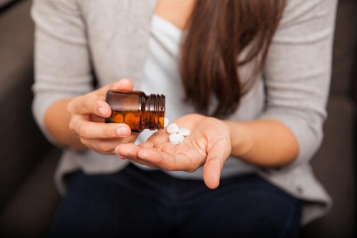 Stock image of woman pouring pills into her palm from a bottle