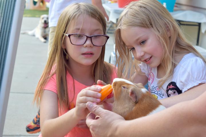 Two girls, one holding a guinea pig and the other feeding it a carrot