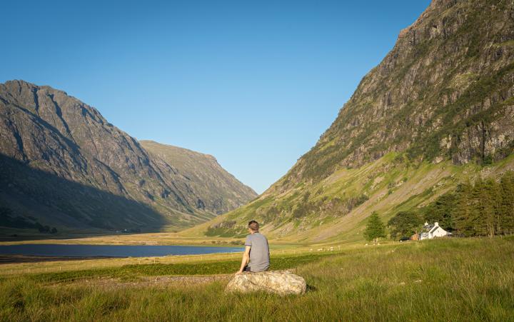 Man sitting on a rock on his own facing a loch in Glencoe