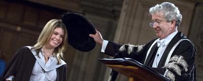 The prinicipal doffing the head of a student with the geneva bonnet to confer his degree