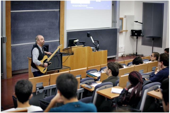 A lecturers uses a guitar to teach his students