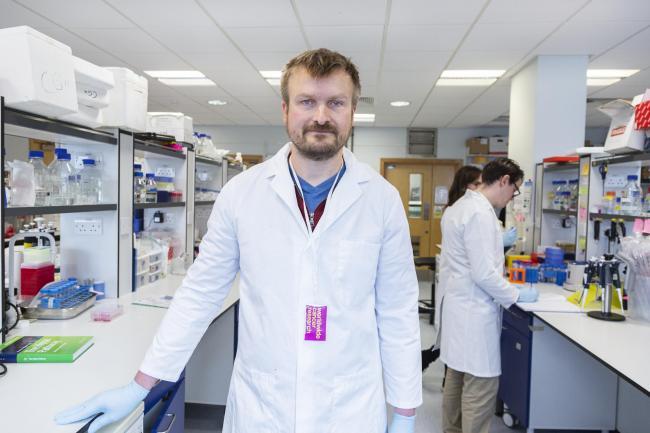 Dr Carsten Hansen standing in a lab, wearing a white lab coat