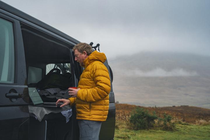 Mature man catches up with some work on his laptop whilst in his campervan in the Scottish Highlands
