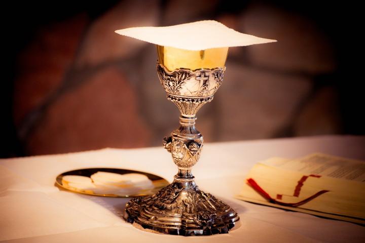 Photograph of a goblet on a table, a plate with bread and a book to the side.