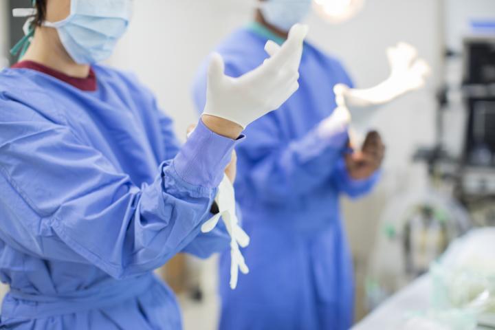 Close up of two doctors putting on protective surgical gloves before performing a procedure in a hospital operating room
