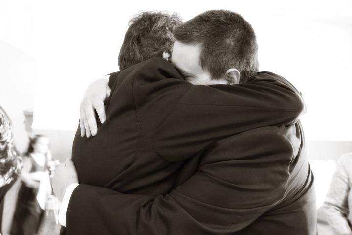 A black and white photograph of two men hugging each other. 