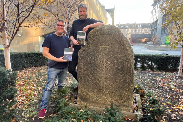 Ian Giles and Chris Cooijmans holding their books by the Swedish Runestone