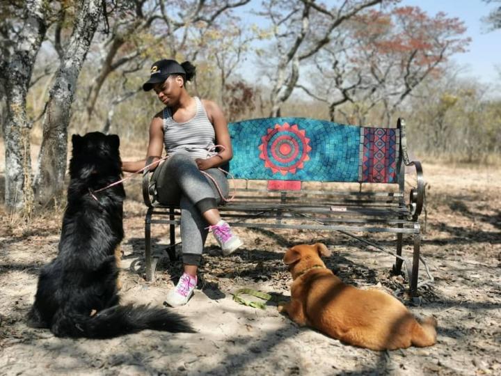 Photograph of Lindiwe Dhlakama sitting on a bench beside two dogs. 