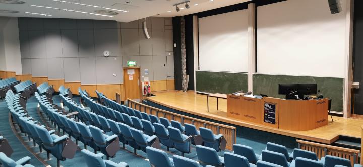 Banked rows of green seats facing a stage with computer desk and projector screens behind