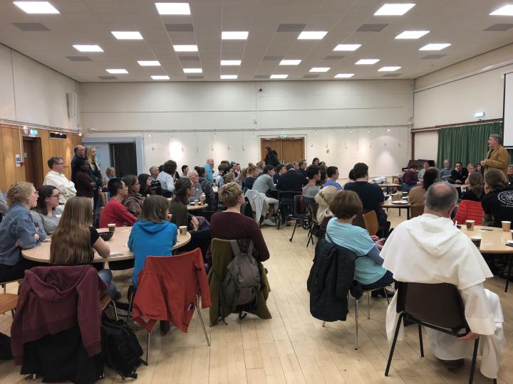 Photograph of a meal being held in the auditorium in The Chaplaincy Centre. There are groups of people sitting talking at tables