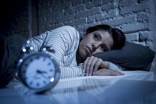 Photograph of a woman lying awake in bed staring at a clock. 
