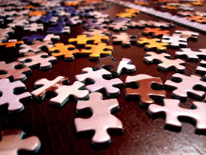 Photograph of different coloured jigsaw pieces lying on a brown table. 