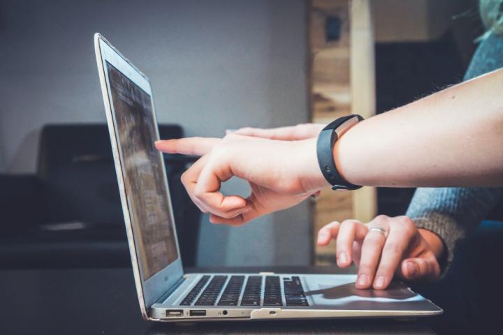 Open laptop, side on view. One hand using mousepad and someone else's hand pointing at the screen