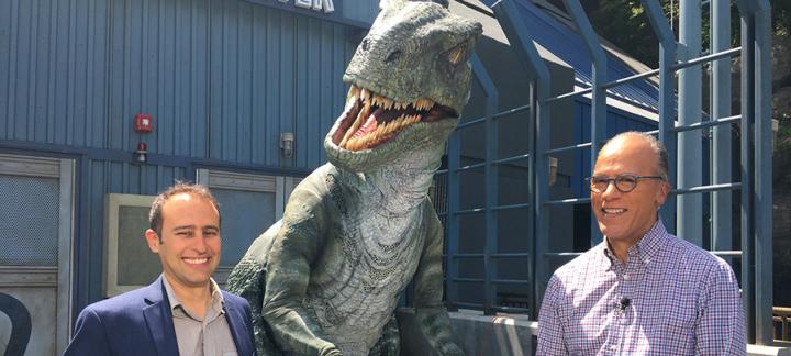 Prof Steve Brusatte and colleague stand next to a life size model of a dinosaur