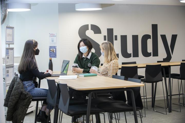 Three students sit at a table with masks on