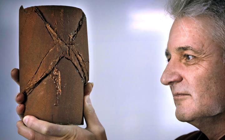 Side profile of Professor Ian Main holding a rock sample that was deformed in the rock lab.