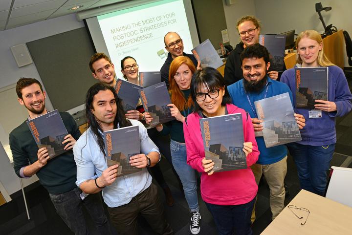 Several people holding up a copy of the postdoc handbook.