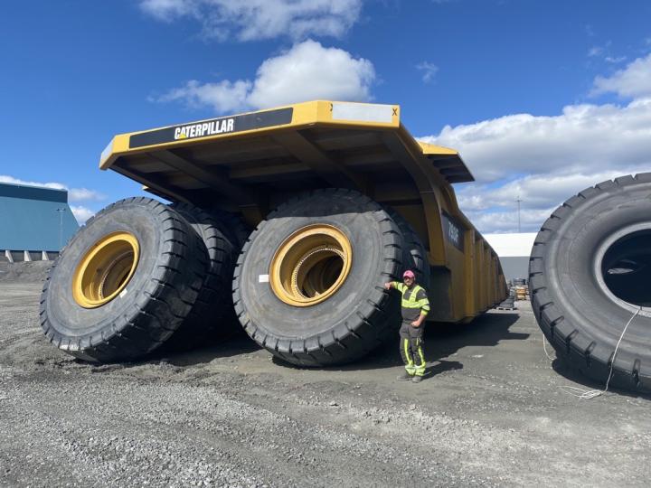 David stands leaning against a Caterpillar vehicle with enormous wheels - they are double his height