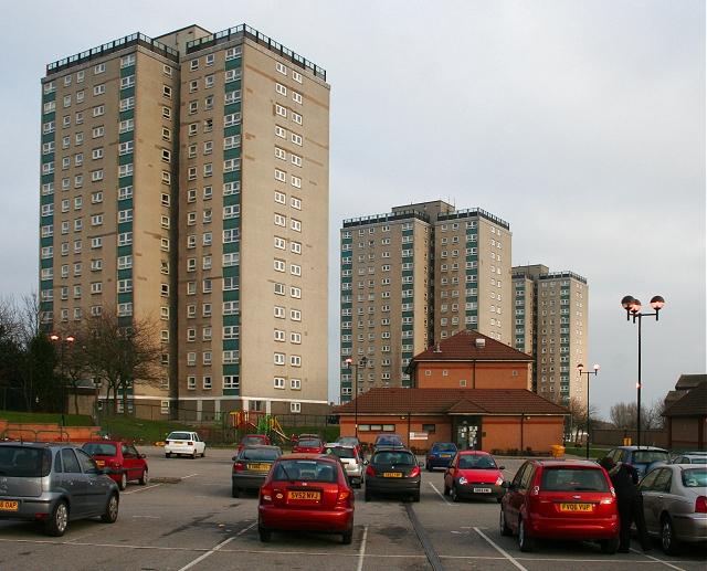 Image showing three tower blocks, high-rise in a pale beige-yellow colour cladding, behind a car park. 