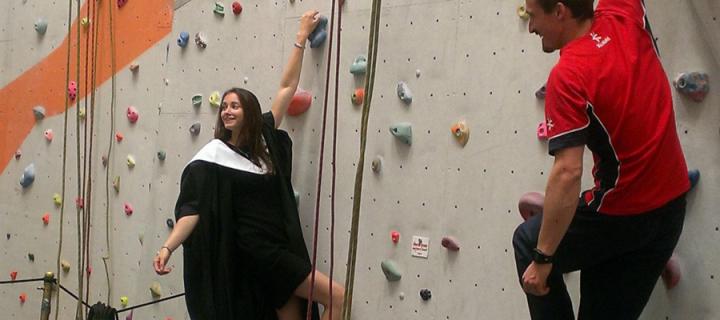 Natalie Berry on the climbing wall in her graduation robe