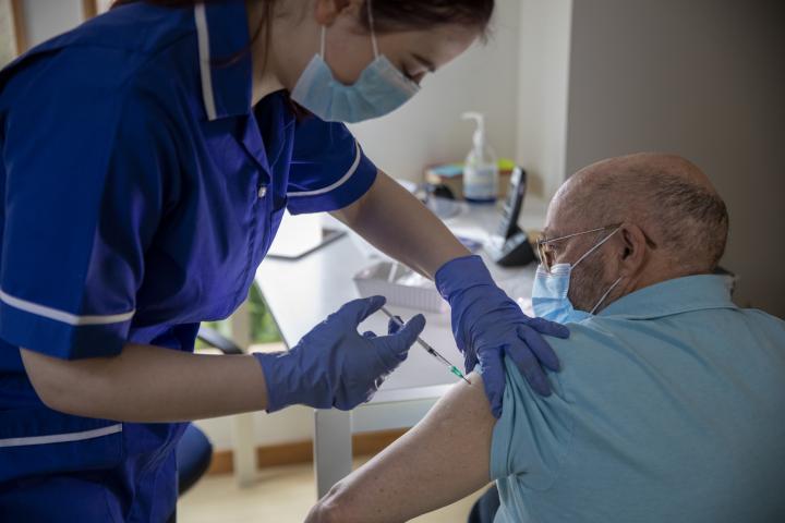 A nurse putting a vaccine in a man's arm who is sitting down