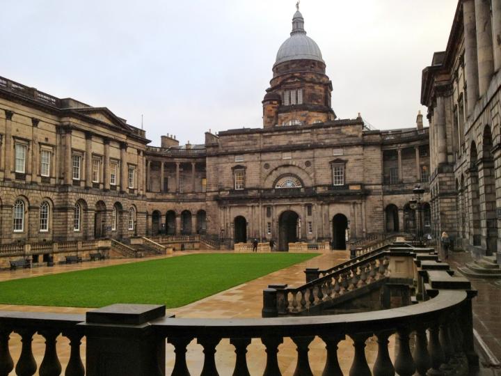 Photograph of Old College Quad. There is a rectangle of green grass in the centre of the image, with the grey stone Old College building surrounding it. 