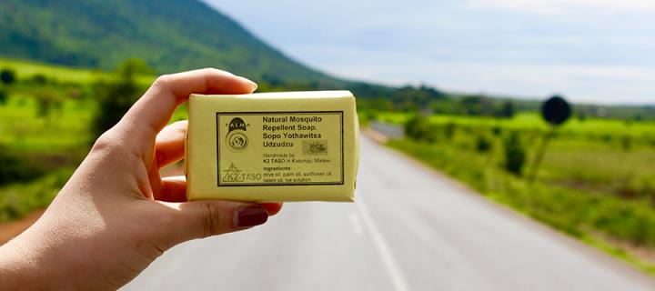Hand holding a palma soap bar with Malawian landscape in the background
