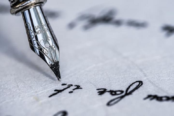 Photograph of a pen writing on a piece of white paper. 