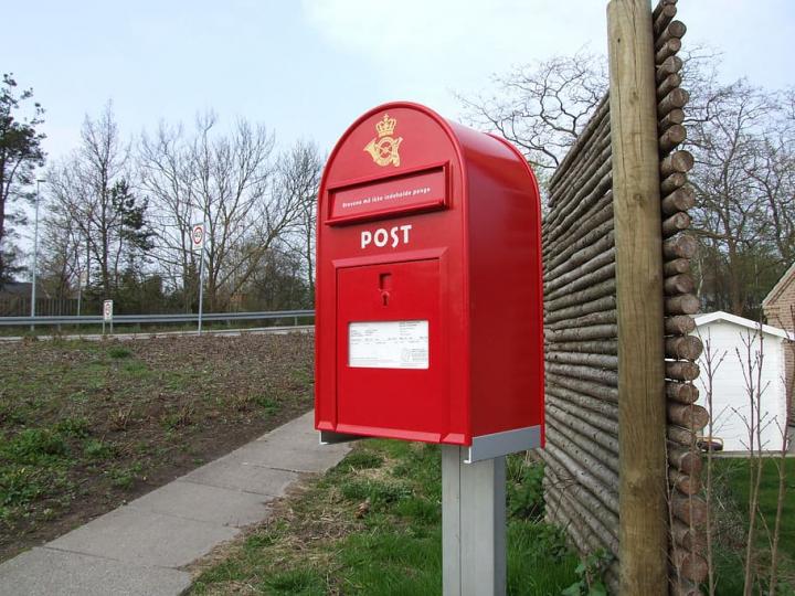 Photograph of a red postbox beside a path and a park. 