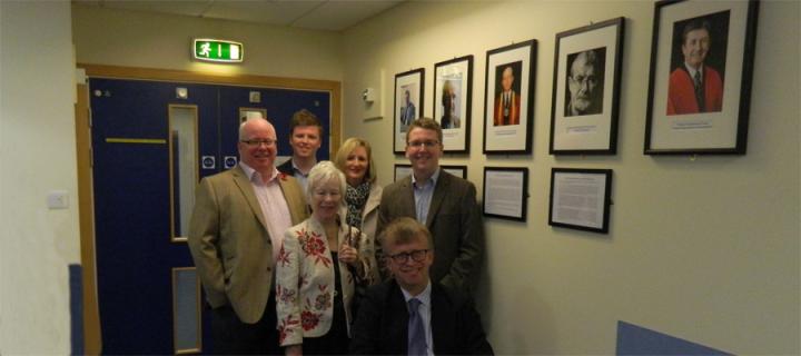 Prof's Spence's family pose with the portraits of the past Heads of Department