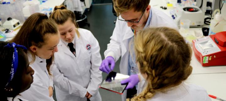 A PhD student explains a laboratory technique to school pupils