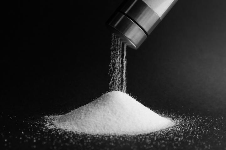 A pile of salt on a black background with a salt shaker above pouring more salt on