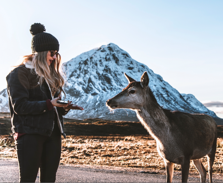 A woman next to a female deer, in front of a snow covered mountain