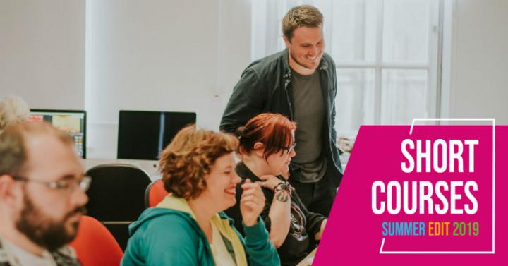 Students behind computer desks with tutor smiling beside them. Summer Edit 2019 logo in lower right-hand corner.