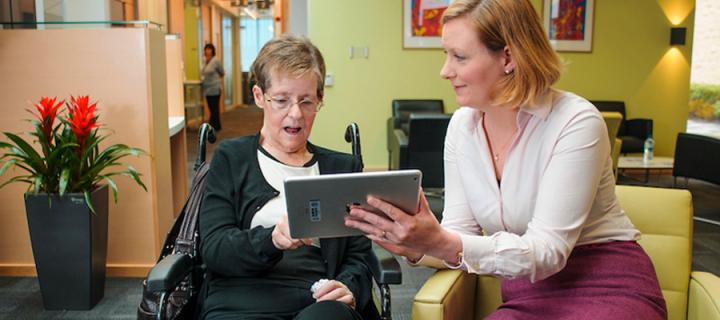 a researcher helping a woman with motor neurone disease complete an assessment on an iPAD