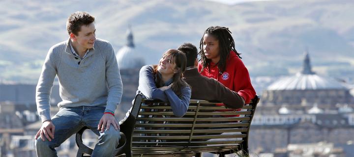 Students sitting on a bench on Carlton Hill with the city in the background
