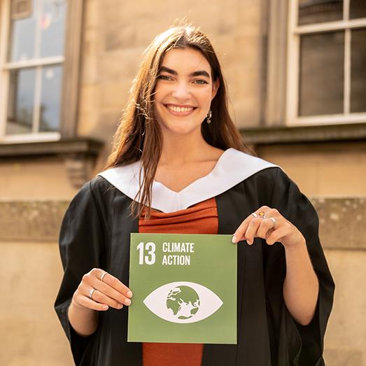 Student at graduation holding Climate Action Sustainable Development Goal 13 card