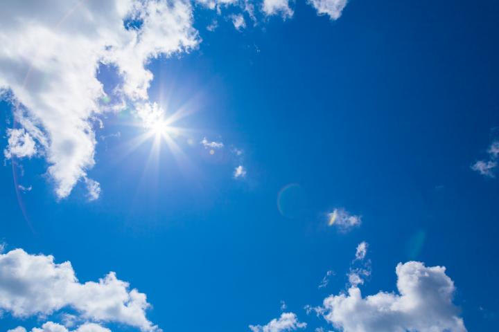 Photograph of the sun shining in the blue sky, with a few white clouds dotted around