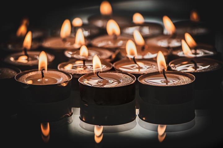 Photograph of a group of lit tealights, the tealight holders are black and lying on a dark table. 