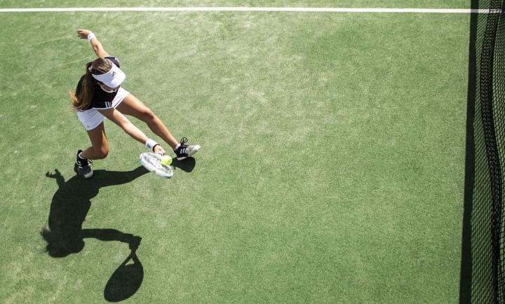 Overhead photograph of a woman playing tennis on a grass court. The woman is wearing black shorts and a black top