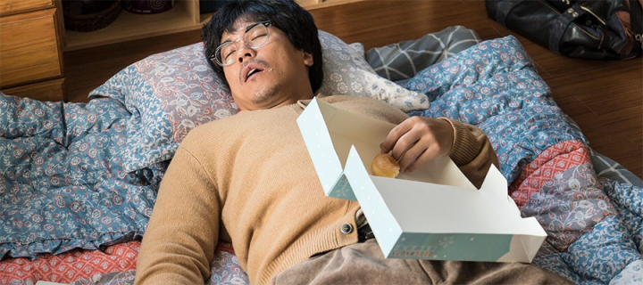 Still from a film showing a man asleep holding a box of doughnuts