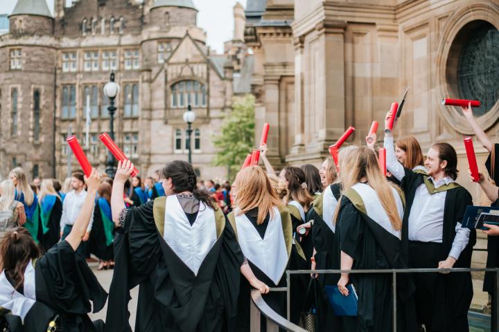 Image of a group of students in academic robes celebrating their graduation outside of McEwan Hall