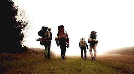 Photograph of 4 people walking away from the camera along a path. The four people have large hiking rucksacks on their backs. 