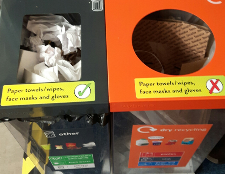 General waste and recycling bins with stickers on them about how to properly dispose of paper towels, face masks and wipes.