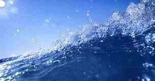 A close up photograph of a wave with blue skies overhead.