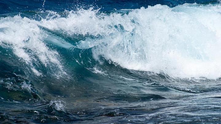Close up photograph of waves crashing, blue waves with white spray from the wave. 